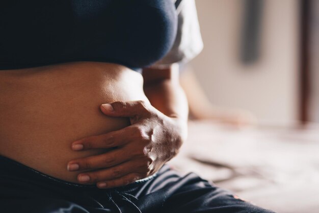 Foto seção média de uma mulher grávida sentada com as mãos no estômago em casa