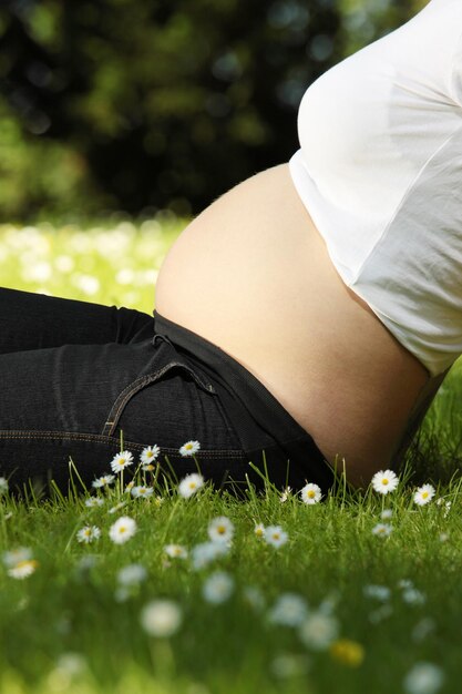 Seção média de uma mulher grávida sentada em um campo de grama no parque