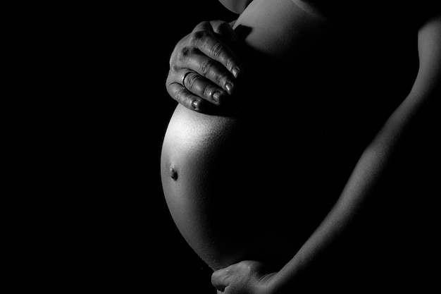 Seção média de uma mulher grávida tocando a barriga contra um fundo preto