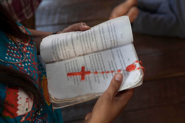 Seção média de uma mulher orando com um livro e contas de rosário na capela