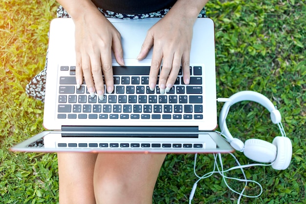 Foto seção média de uma mulher usando um laptop enquanto estava sentada em um campo de grama no parque