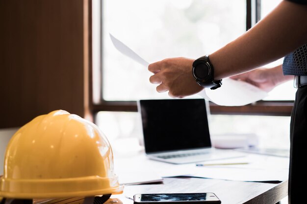 Foto seção média do arquiteto segurando o plano por laptop e smartphone na mesa