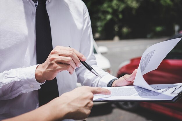 Foto seção média do cliente apontando para o contrato enquanto o agente de seguros segura o caderno