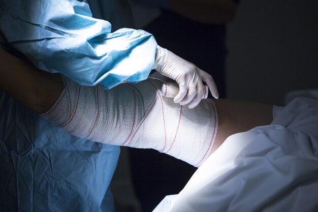Seção média do médico aplicando bandagem na perna do paciente no hospital