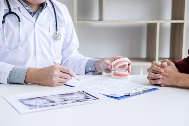 Seção média do médico mostrando dentaduras enquanto explica a receita ao paciente na mesa
