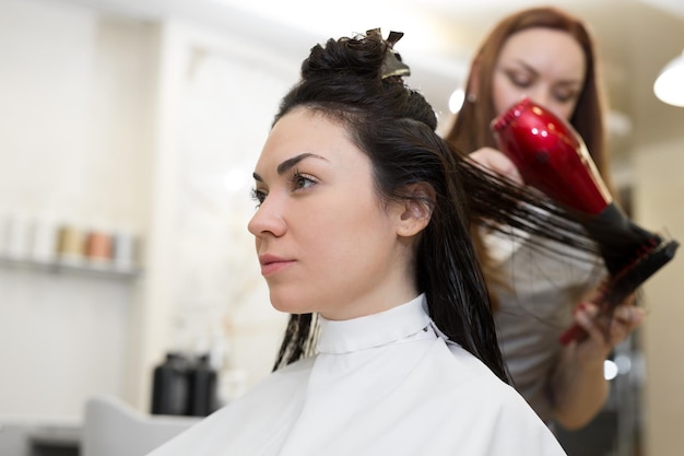 Secar el cabello largo y castaño con secador de pelo y cepillo redondo.