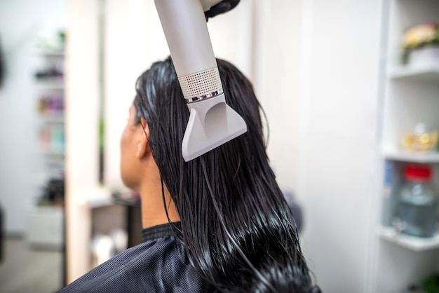 Secar cabelos longos e escuros com um secador de cabelo cabeleireiro profissional seca o cabelo de um cliente no salão de beleza penteado beleza cuidados com o cabelo serviço de moda