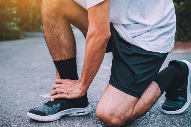 Foto sección baja del atleta atando el cordón de los zapatos en la carretera