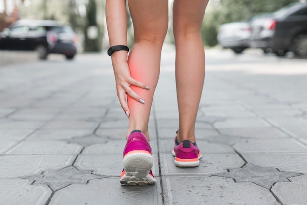 Foto sección baja de atleta femenina de pie en la calle con dolor en la pierna