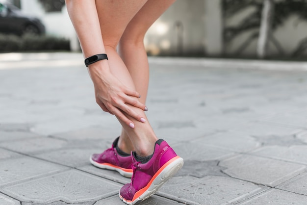 Sección baja de atleta femenina de pie en la calle con dolor en el tobillo