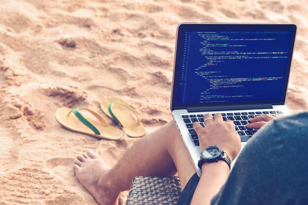 Sección baja de un hombre adulto medio usando una computadora portátil mientras está sentado en la playa