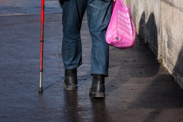 Sección baja de un hombre caminando con bolsa y bastón en la calle