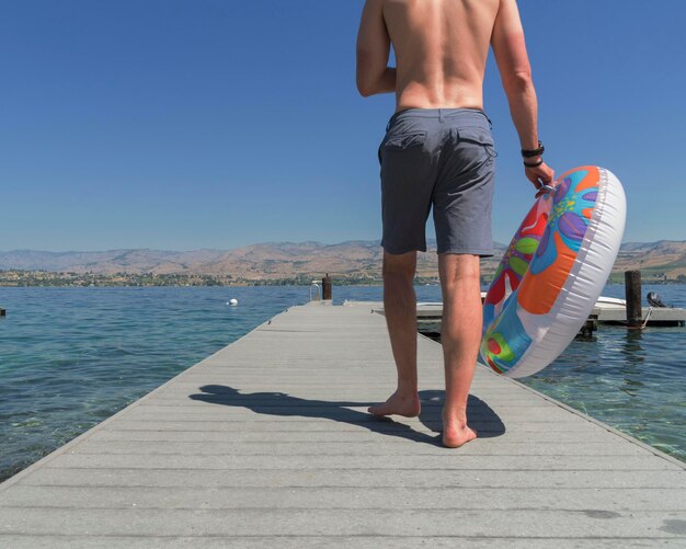 Foto sección baja de un hombre caminando por el muelle sobre el lago