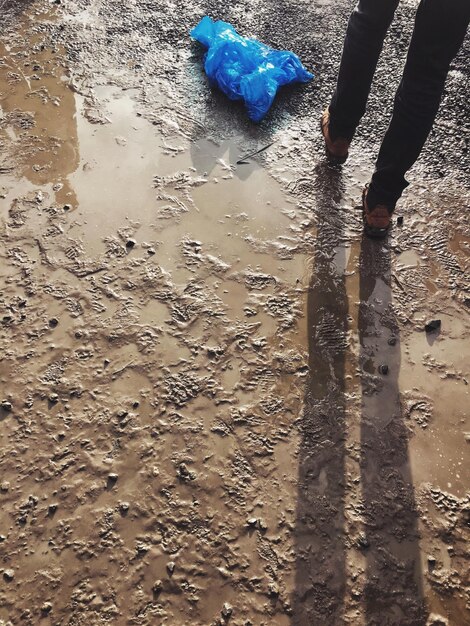 Sección baja de un hombre caminando sobre arena húmeda en la playa