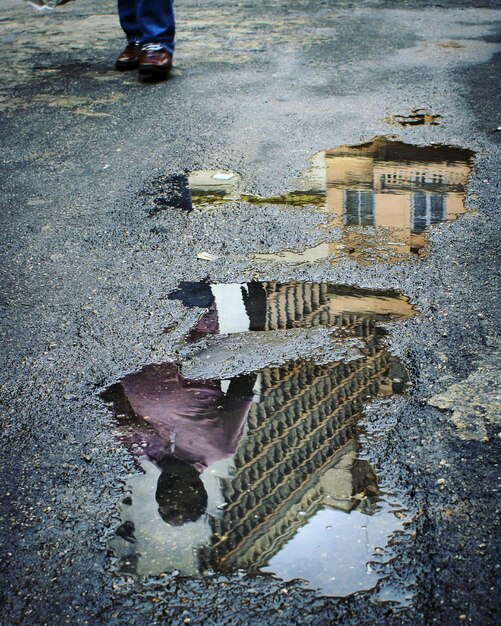 Sección baja del hombre por el charco con reflejo en la ciudad