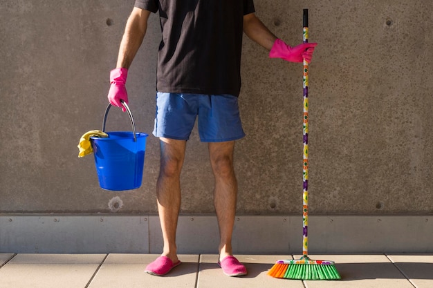 Sección baja del hombre con equipo de limpieza de pie contra la pared