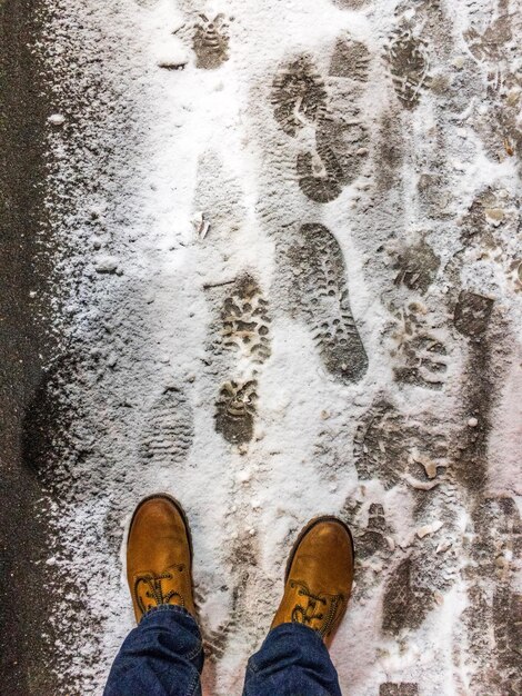 Sección baja de un hombre de pie en una carretera cubierta de nieve