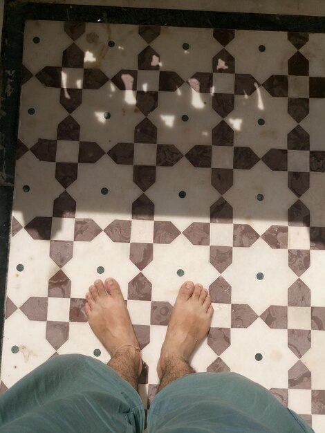 Foto sección baja de un hombre de pie en un piso de azulejos