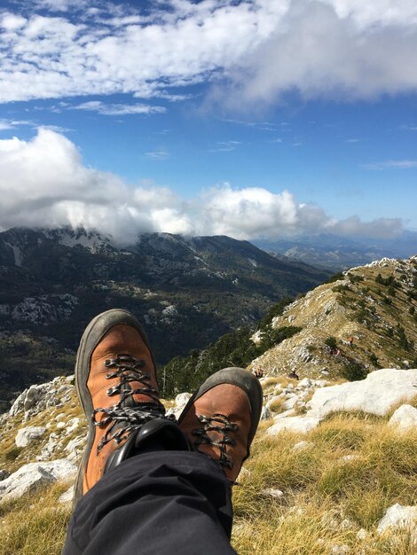 Foto la sección baja del hombre de pie en las rocas contra las montañas momento zen ver las nubes meditación