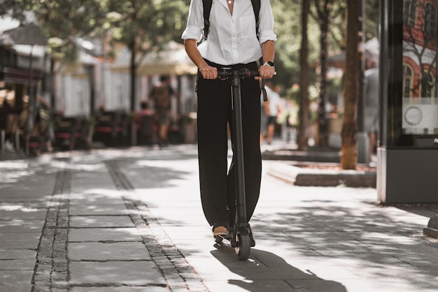 La sección baja del hombre de pie sobre el scooter de empuje en la acera