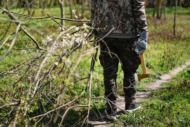 Sección baja de un hombre que lleva ramas cortadas y un hacha en el bosque