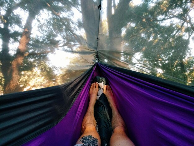 Foto sección baja de un hombre relajándose en una hamaca contra los árboles