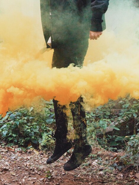 Foto sección baja de un hombre saltando en medio del humo sobre el campo