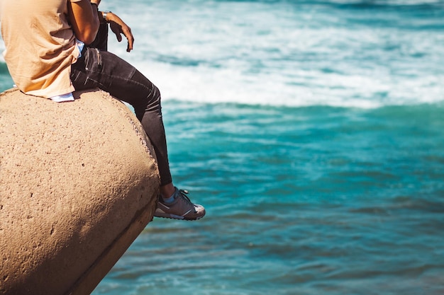 Sección baja de un hombre sentado en una roca sobre el mar