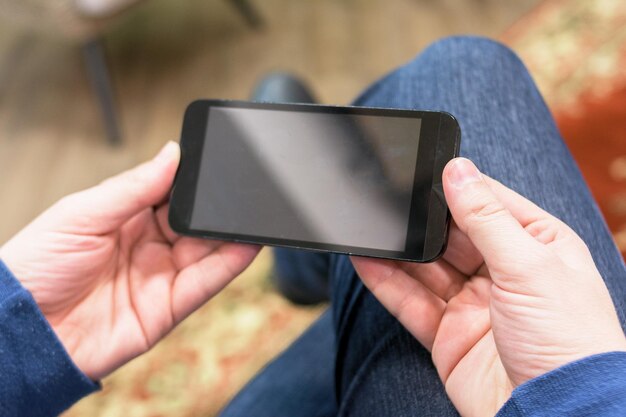 Foto la sección baja del hombre usando el teléfono móvil mientras está sentado en casa