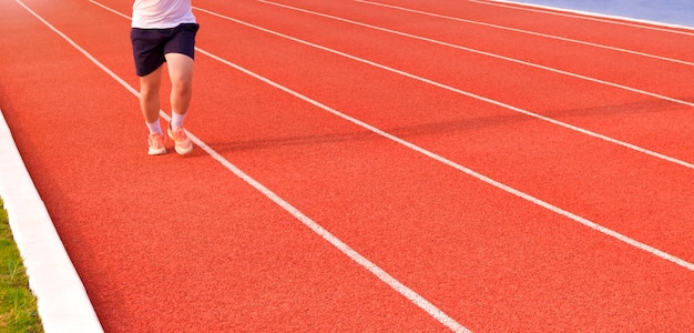 Sección baja de un joven trotando en una pista de atletismo en un estadio al aire libre con vistas panorámicas