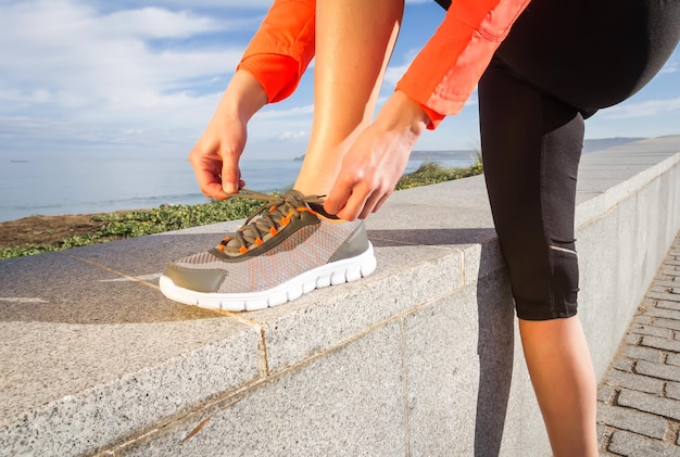 Sección baja de la mujer atando el cordón de los zapatos contra el cielo