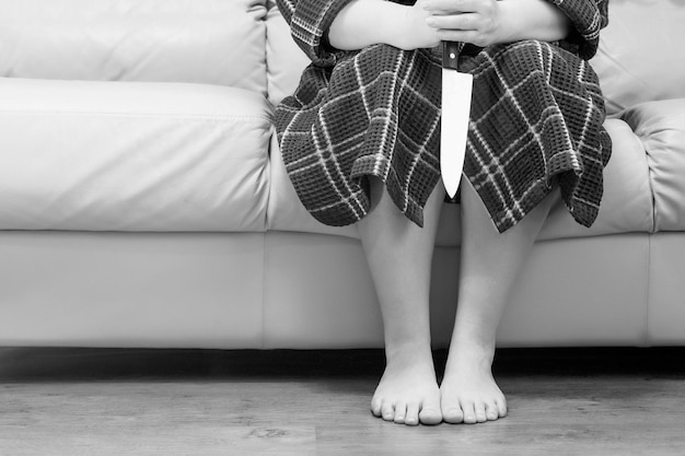 Sección baja de una mujer con un cuchillo sentada en el sofá en casa