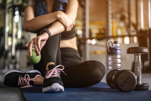 Foto sección baja de una mujer con frutas sentada en el gimnasio