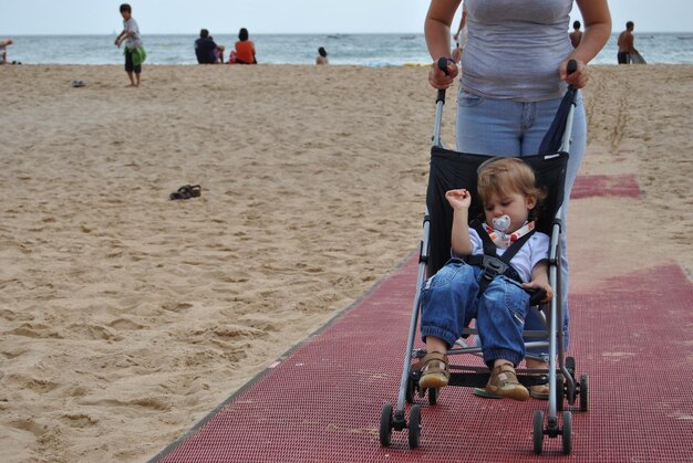 Foto sección baja de una mujer con un hijo en un cochecito de bebé en la playa