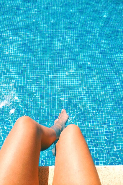 Foto sección baja de una mujer joven relajándose a orillas de la piscina en un día soleado