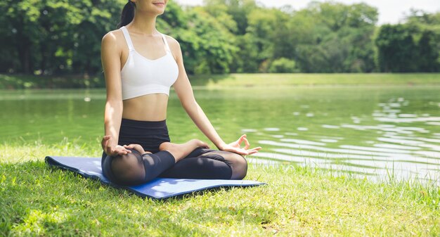 Foto sección baja de una mujer meditando junto al lago