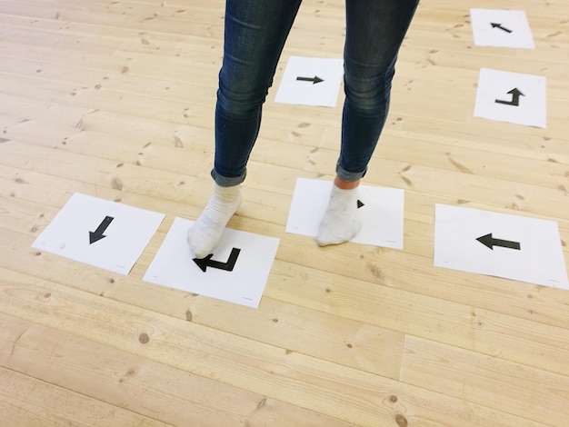 Sección baja de una mujer de pie sobre símbolos de flecha en el suelo de madera dura