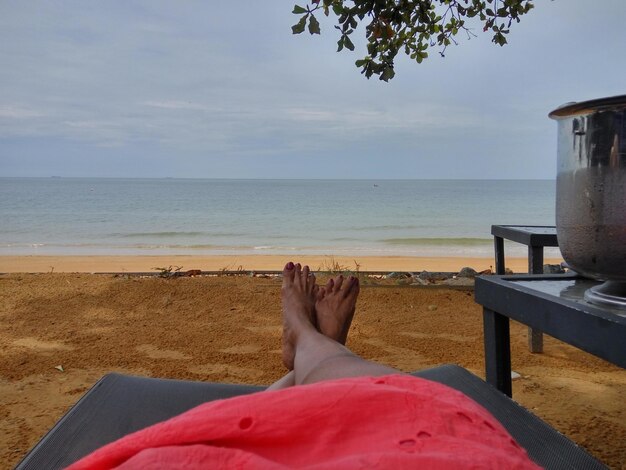 Foto sección baja de una mujer relajándose en la playa contra el cielo