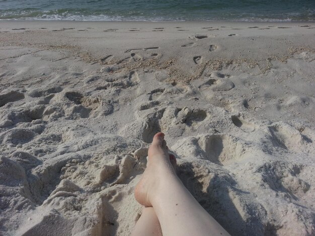 Foto sección baja de una mujer sentada en la arena de la playa