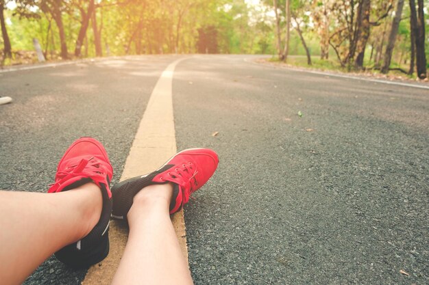 Sección baja de la mujer sentada en la carretera contra los árboles