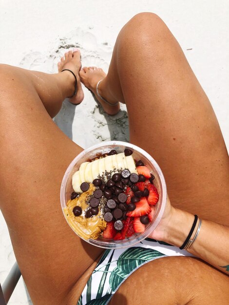 Foto sección baja de una mujer sosteniendo frutas en la playa durante un día soleado