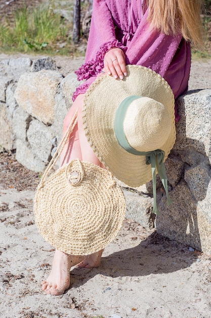 Sección baja de una mujer sosteniendo un sombrero de sol mientras está sentada en una pared de piedra