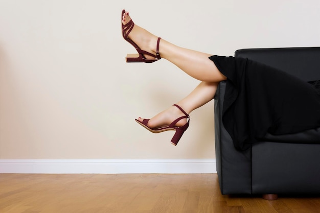 Foto sección baja de una mujer con tacones altos acostada en el sofá en casa