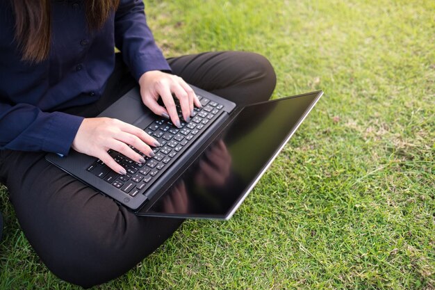 Sección baja de una mujer usando una computadora portátil sentada en la hierba en el parque.