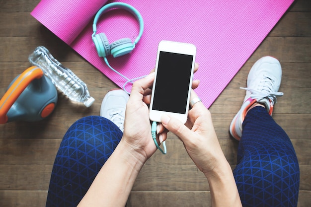 Sección baja de mujeres que usan teléfonos móviles haciendo ejercicio en el suelo en casa