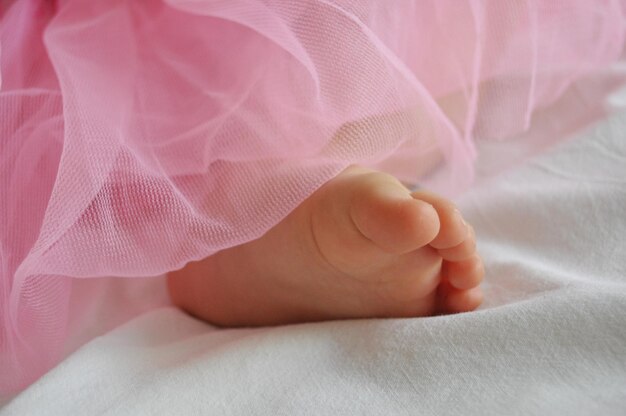 Foto sección baja de una niña en vestido rosa en la cama