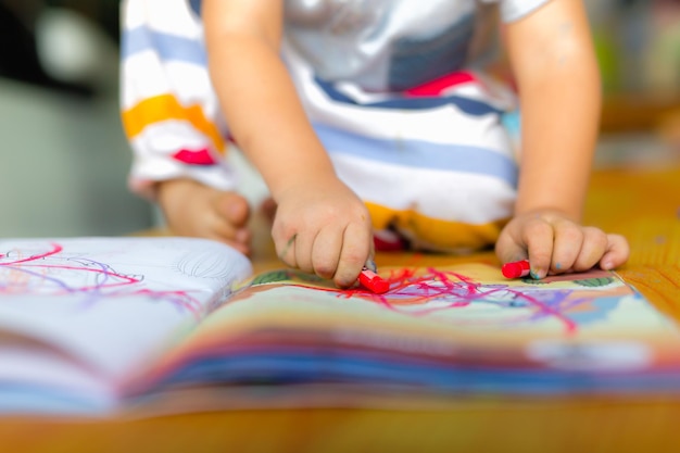 Sección baja de un niño con un libro en la mesa en casa