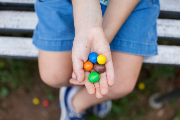 Foto sección baja del niño sosteniendo dulces coloridos mientras está sentado en el banco