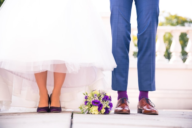 Foto sección baja de la novia y el novio con un ramo de flores de pie en el suelo