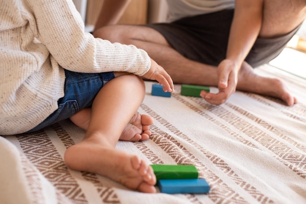 Foto sección baja de padre e hija jugando con bloques de juguete en la cama en casa